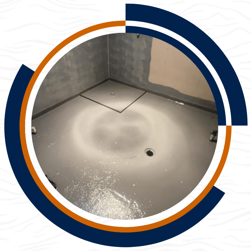 Waterproofing on a freshly coated grey floor with a drain and marked area prepared for tiling.